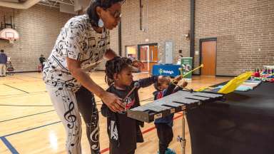 Mom and children playing with a xylophone in a community center gymnasium.