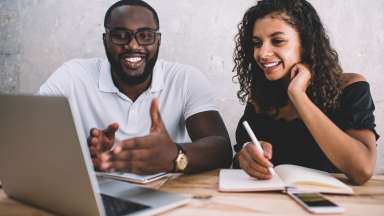 Man and woman viewing laptop screen and taking notes