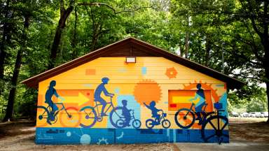 colorful mural of a people riding bikes on a picnic shelter wall.