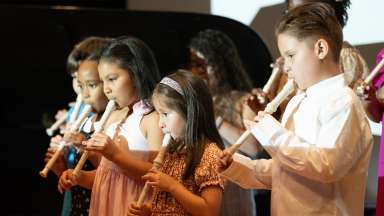 Children of varying ages on a stage playing recorders