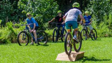a group of kids on bikes wearing helmets and one is jumping off a wooden ramp