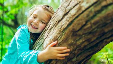 a child outside happily  hugging a tree