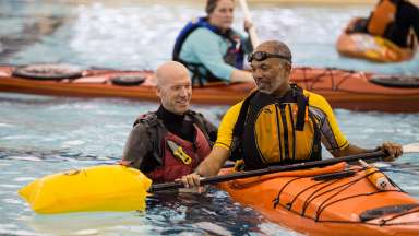 an person showing another how to paddle in a kayak in a swimming pool