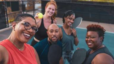 A group of people on a pickleball court with balls and a paddle