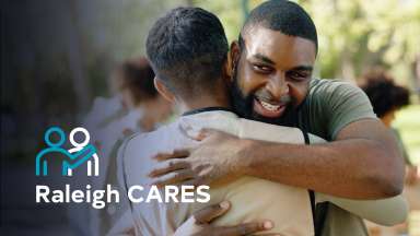 A man hugging another man with the Raleigh CARES logo overlaid on the photo