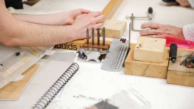 Hands working with metal and art supplies in the Sertoma studios.