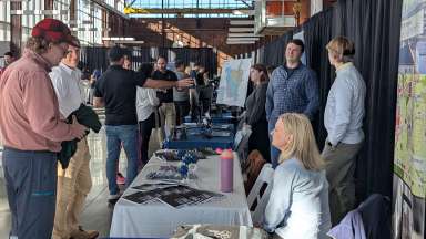 GIS Day event photo from 2024. People talking at participant tables.