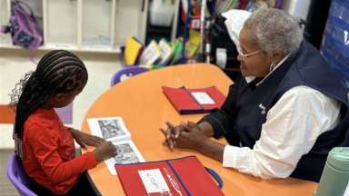 Foster grandparent sitting at desk with student