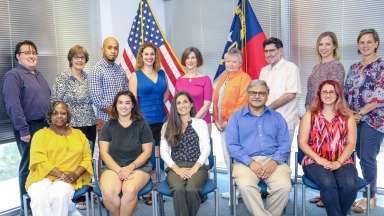 14 people posing in front of American flag and NC flag