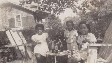Three young girls have a tea party in a historic black and white image.