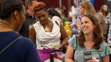 A brown-haired woman smiles at the 2025 Small Business Expo while speaking to other community members.