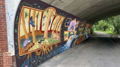A mural within a greenway tunnel, painted with dark colors and depicting flora and fauna