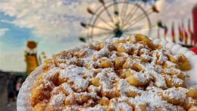 Funnel cake with powdered sugar with blurred fair games in the background