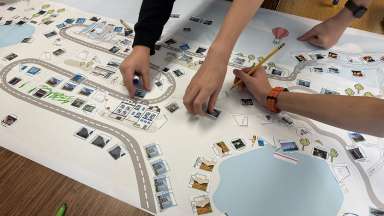 Community Planning Month - Photo of a paper map laid out on a table and people placing paper buildings and things on top of it