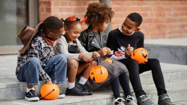 children in costumes sitting on the stairs with orange pumpkin containers