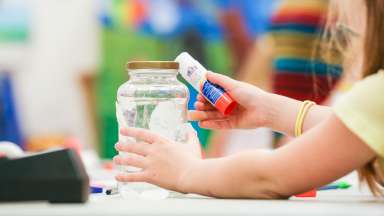 Photo of young child creating art with a glue stick and jar and paper