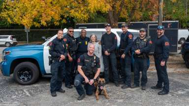 Ms. Parker stands with several officers including a officer and K9. A police cruiser is behind the group