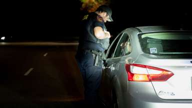 At night, a Raleigh police officer stand by the driver side of a car talking with the driver.