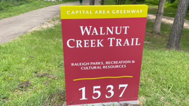 Walnut Creek Trail Trailhead ID Sign on grass in front of the greenway trail