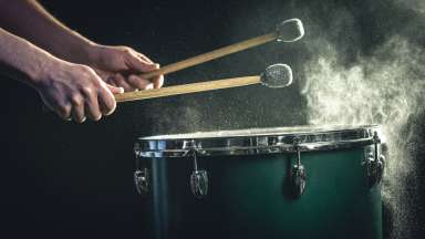 The percussionist plays with sticks on the floor tom on under studio lighting