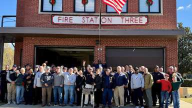 active and retired Raleigh firefighters showed up to celebrate the station before it closes in early 2026. the group is standing in front of the building's two garage bays. There's a flag pole with the tip of the American Flag showing at the top of the photo.