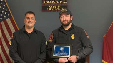 Two officers stand in front of the North District, Raleigh, NC sign. One officer holds a plaque.