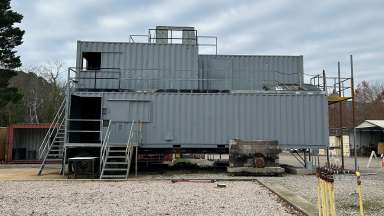 The two story structure is made of metal shipping containers and has a front staircase and windows.