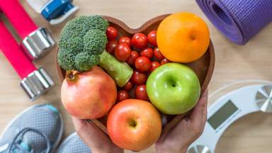 Heart-shaped bowl of fruit and vegetables surrounded by other exercise equipment