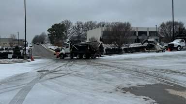 a road covered in winter precipitation, with a dump truck with a snow plow leaving down the road