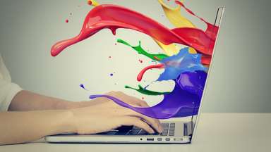 a person's hands typing on a laptop with colorful paint coming out of the screen
