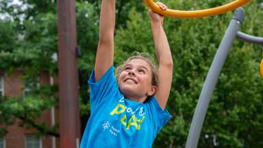 a child on hanging on a play structure at summer camp