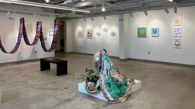 A wide view of a gallery space showing photographs and paintings hanging on walls