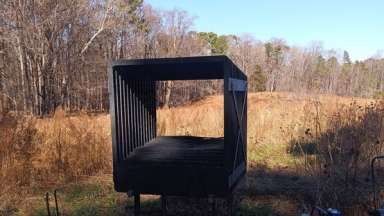 A large, scope-like structure stands at the edge of a meadow, oriented toward an open view of the prairie.