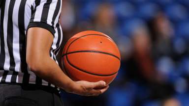 basketball referee holds ball in one hand