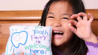 a child holder their tooth and a pillow that says "the tooth fairy is welcome here!"