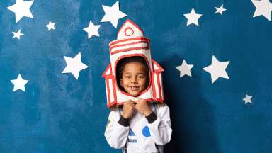 little kid in space suit playing astronaut on blue backdrop with stars