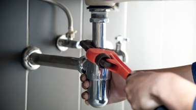 Hand repair under sink leak with red wrench