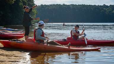 two people in a kayak while one is teaching on the shoreline