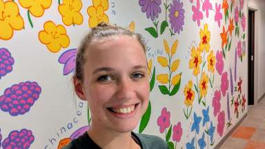 The artist stands in front of her wildflower mural