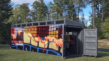A colorful shipping container, covered in artwork, rests in an outdoor setting