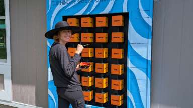A woman wearing dark clothing stands in front of an interactive poetry sculpture
