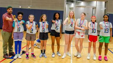 a group of smiling girls and their coach wearing championship medals and rings