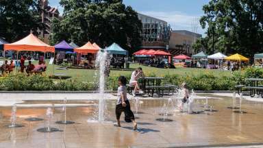 a child playing in the splash pad at Moore Square during an event with tents in the background