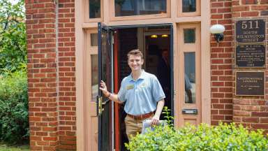 a smiling adult volunteer opening a door at the Pope house museum
