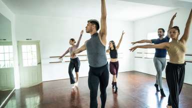 five people in a dance studio standing on one leg with a hand in the air