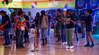 People dancing together at a colorful indoor community party with neon lights and balloons.