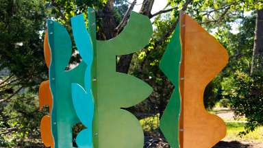 Three metal sculptures in bright greens, blues, and tan