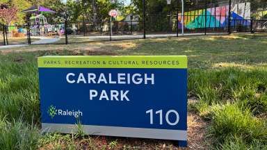 Closeup of a sign saying Caraleigh Park. Artwork can be seen in the background.