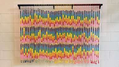 A wall hanging with many vertical rows of rainbow colored beads