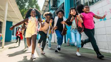 smiling children wearing backpacks and running on a sidewalk